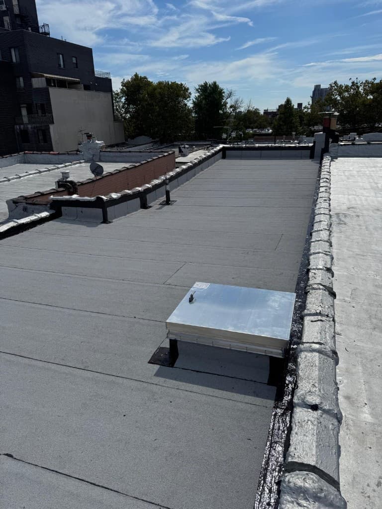 Finished flat roof with a new gray membrane, a metal-clad skylight on a flashed curb and a silver-coated parapet