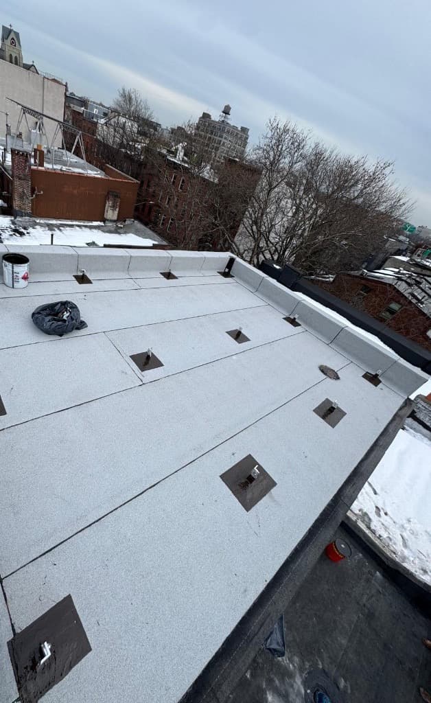 Finished bulkhead roof seen along the parapet, with gray cap sheet laps, metal anchor posts set in black flashed pads and a round roof drain