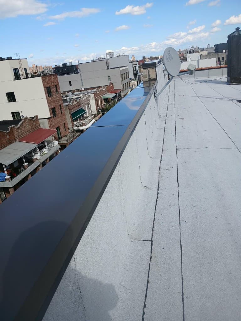 Long run of dark sheet-metal coping along a rooftop parapet, with the gray roof membrane alongside
