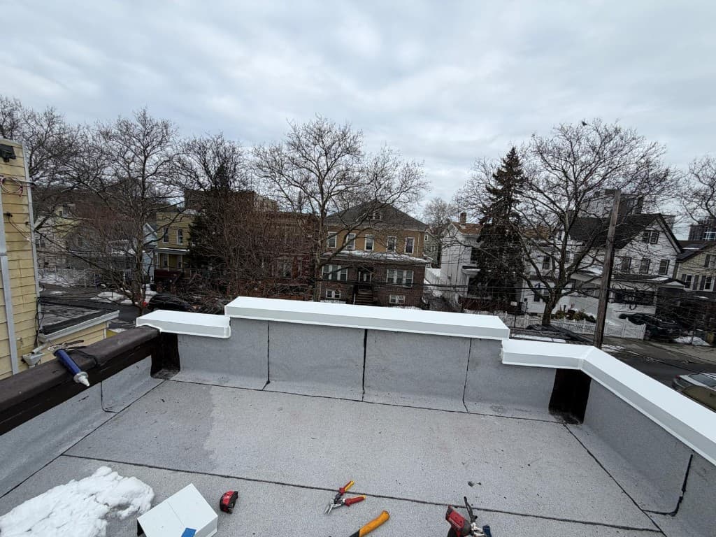 White metal coping installed on membrane-flashed rooftop parapet walls with formed corners and end caps, with tools on the roof