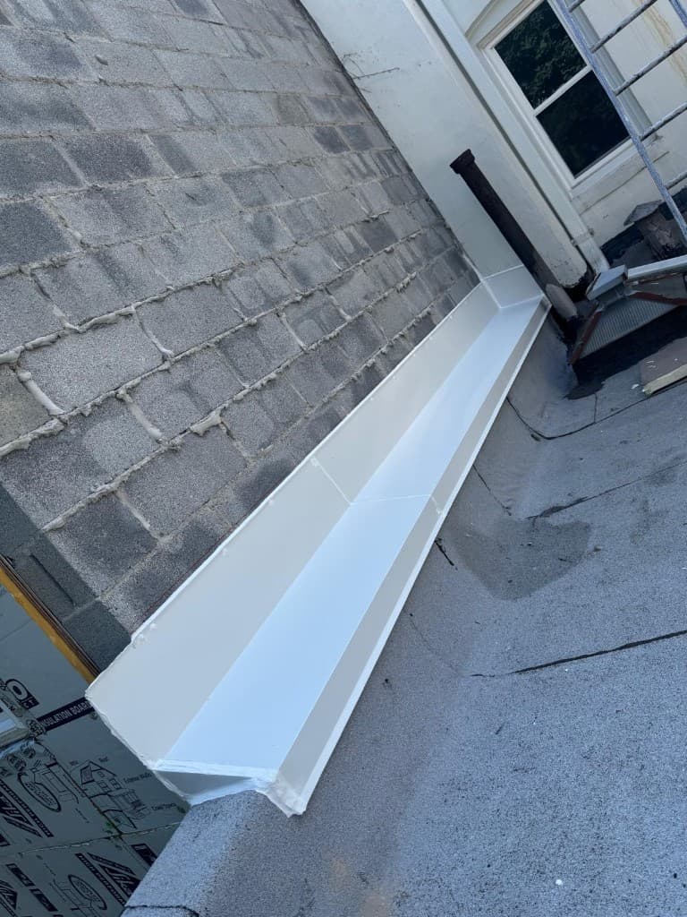 Long custom-formed white metal gutter installed along the base of a wall on a flat roof, with sealed seams and a closed end