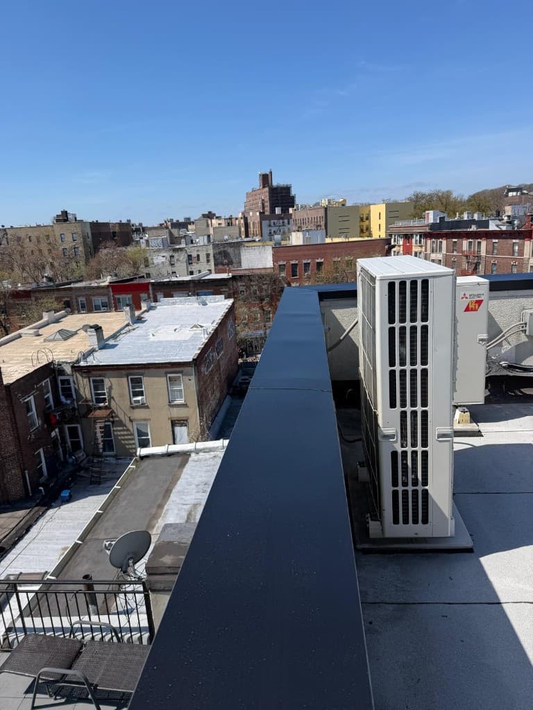 Long dark sheet-metal coping capping a rooftop parapet wall, with the roof membrane running up to it