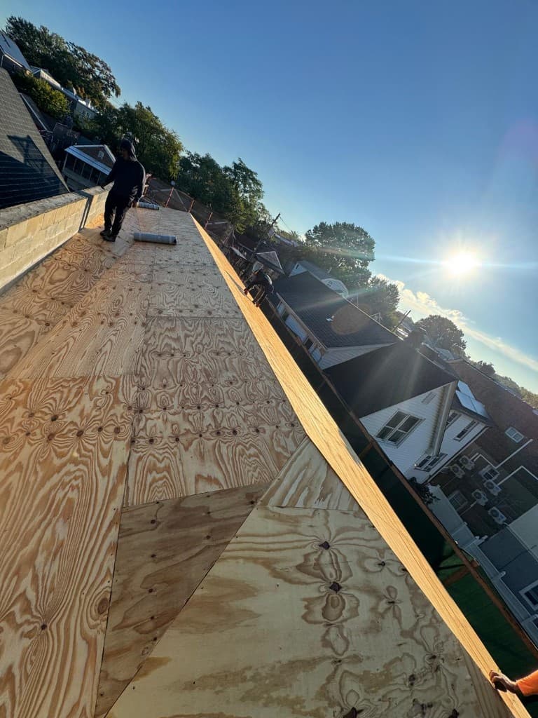 New plywood roof deck installed on a row house roof with a roll of underlayment and a roofer at work