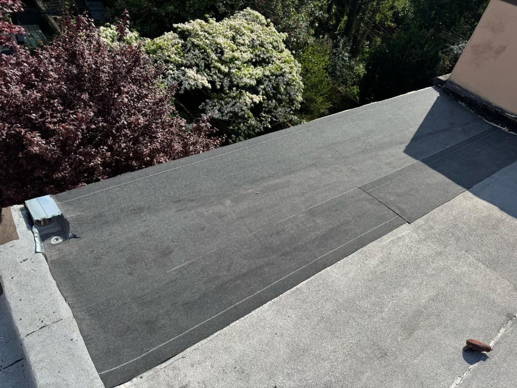 New dark base sheet laid in a repair area on a flat roof with white chalk lines marking the laps, next to a vent with a metal flashing flange
