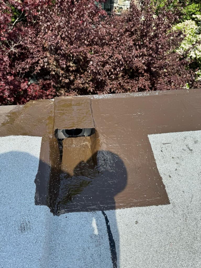 Opening through a parapet wall with its metal flange covered in glossy brown coating on a gray cap sheet roof