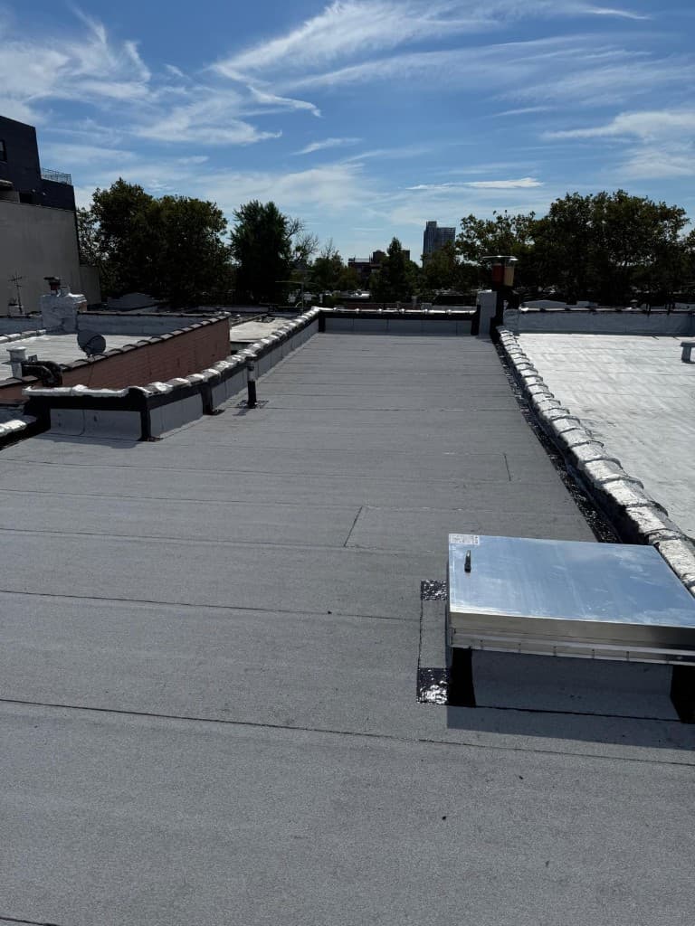 Finished flat roof with a new gray membrane and lapped seams, a metal-clad skylight on a flashed curb and coated parapet caps