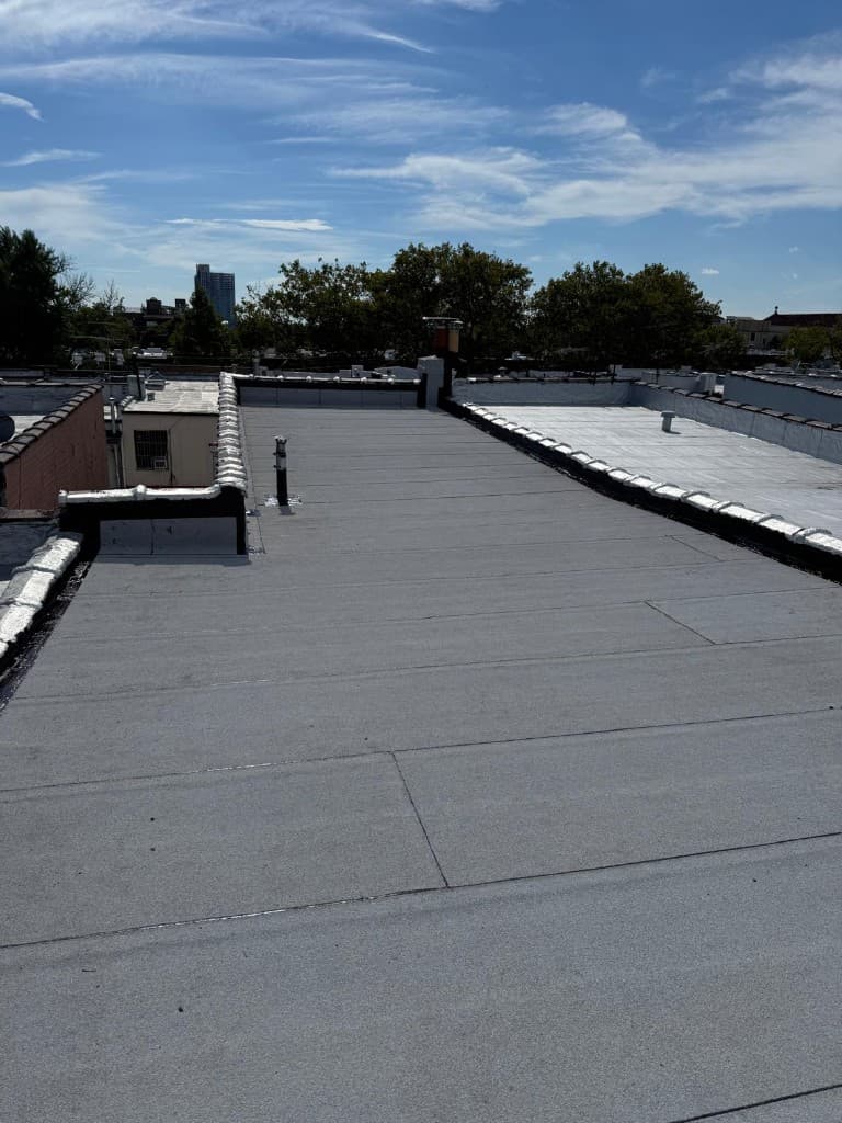 Finished flat roof with a new gray membrane across the whole roof, a flashed vent pipe and white-coated parapet caps