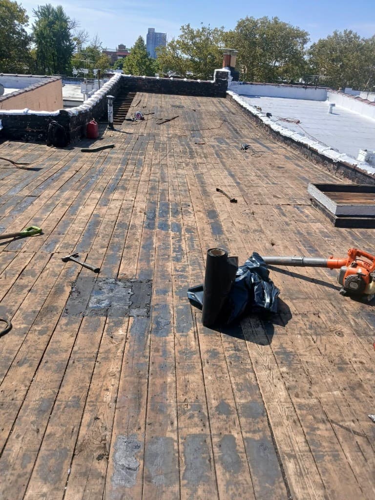 Flat roof torn off down to the original wood plank deck, with a hammer, a leaf blower and an open skylight curb on the roof