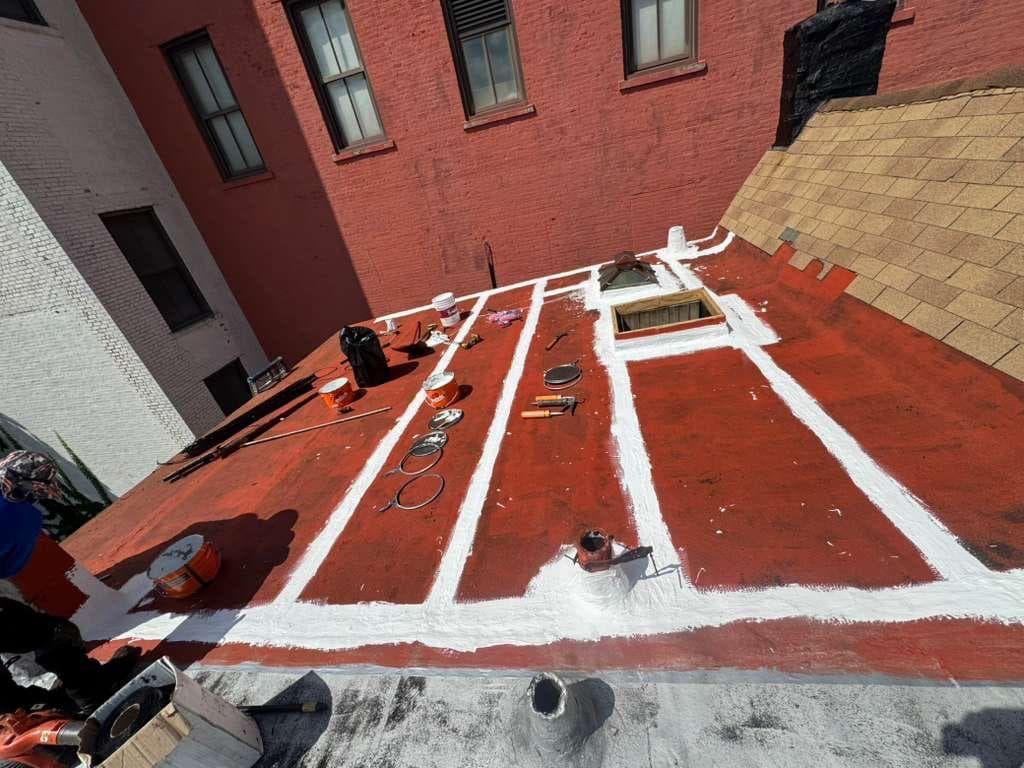 Flat roof with a red base coat and white reinforced coating along seams, a skylight and pipe penetrations