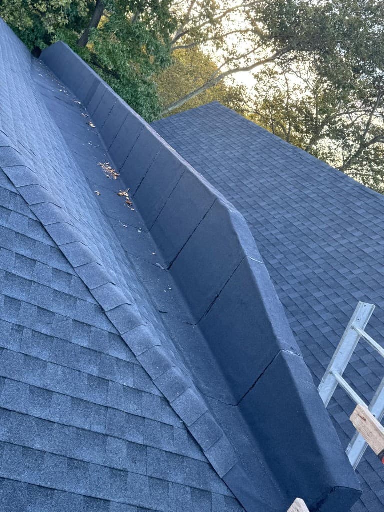 Dark membrane-covered section beside a new shingle slope, with the raised edge built up in angled sections