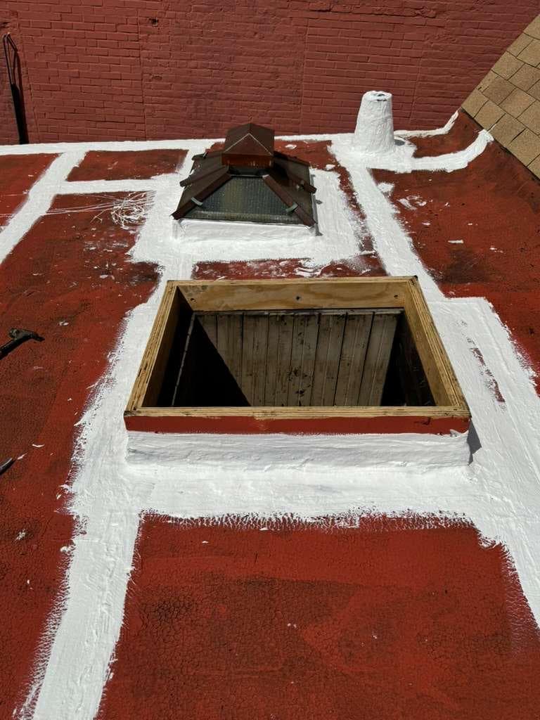Skylight curb and vent pipe sealed with white reinforcing coating on a red base-coated roof