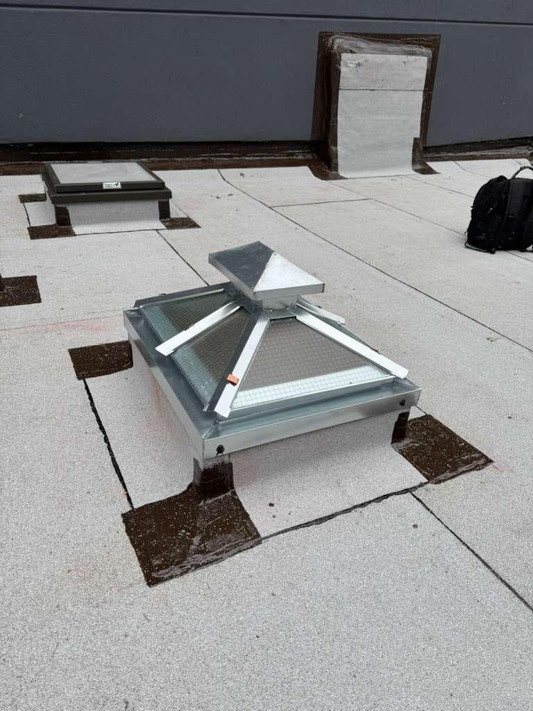 New galvanized pyramid skylight with wired glass on a curb wrapped in cap sheet with brown-sealed corners, a second skylight and flashed wall behind it
