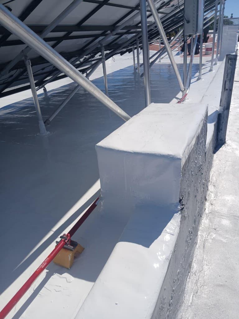 Glossy silicone coating carried over a raised curb and up the parapet, with solar-array legs sealed at their bases