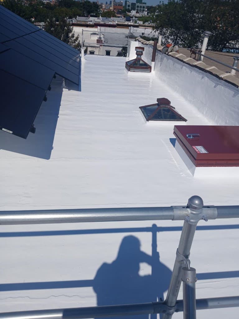 Wider view of the finished white silicone-coated roof with the parapet, skylights, roof hatch and solar array