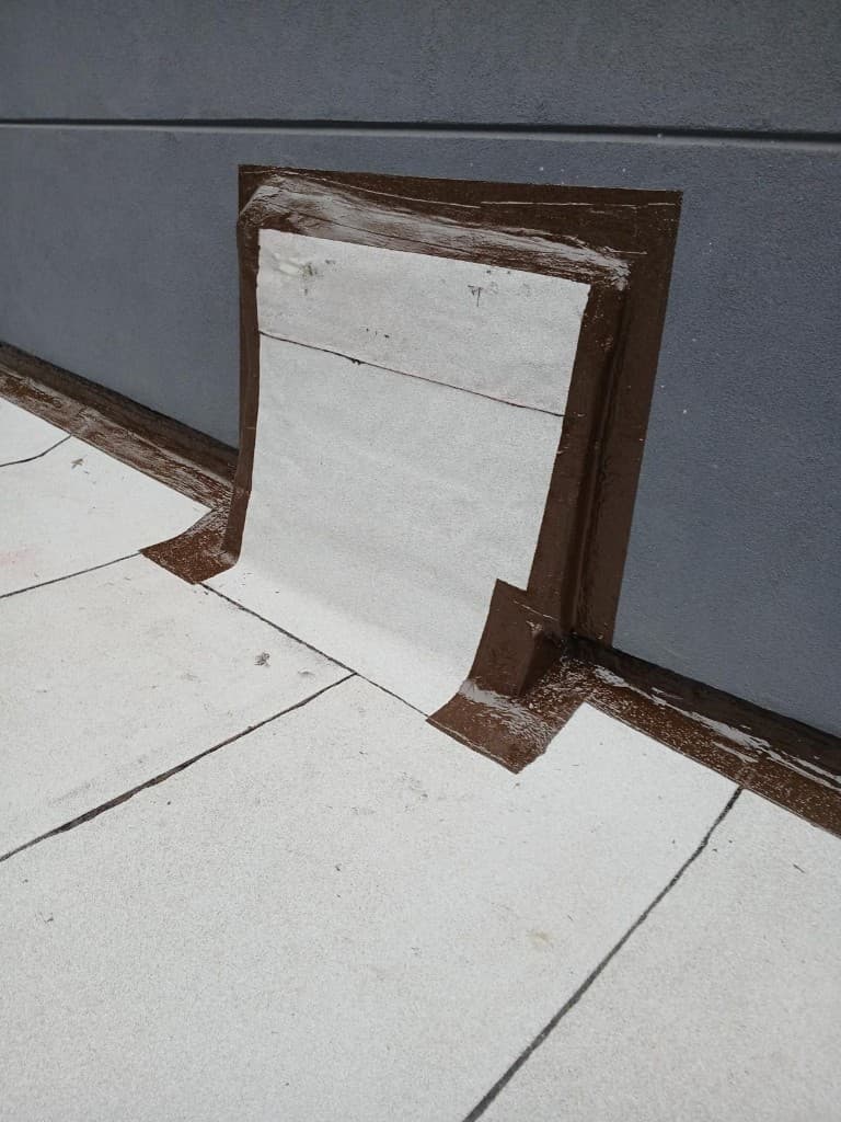 Close view of roofing membrane turned up a gray wall and sealed with brown flashing cement